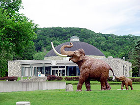 公園に置かれたナウマンゾウのレプリカと記念館（後方）
